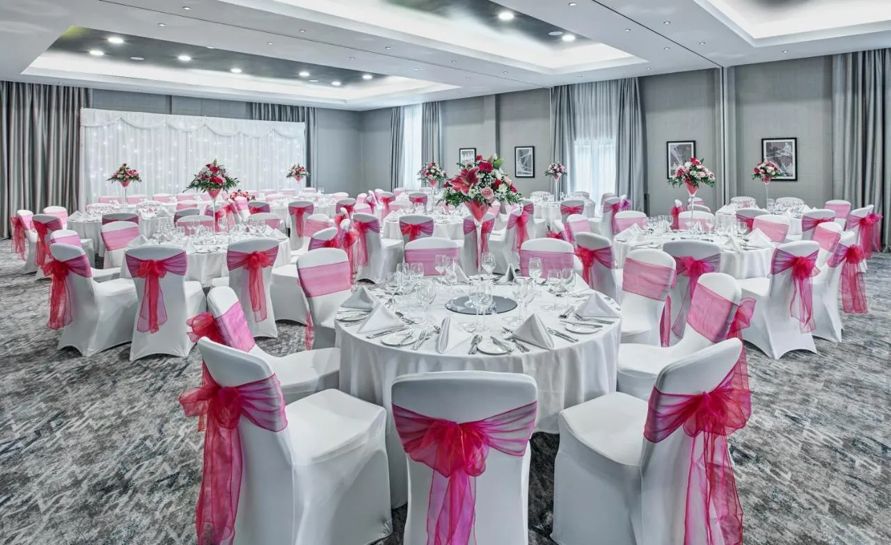 a banquet hall with white tables and pink bows at Leonardo Royal Hotel Oxford in Oxford